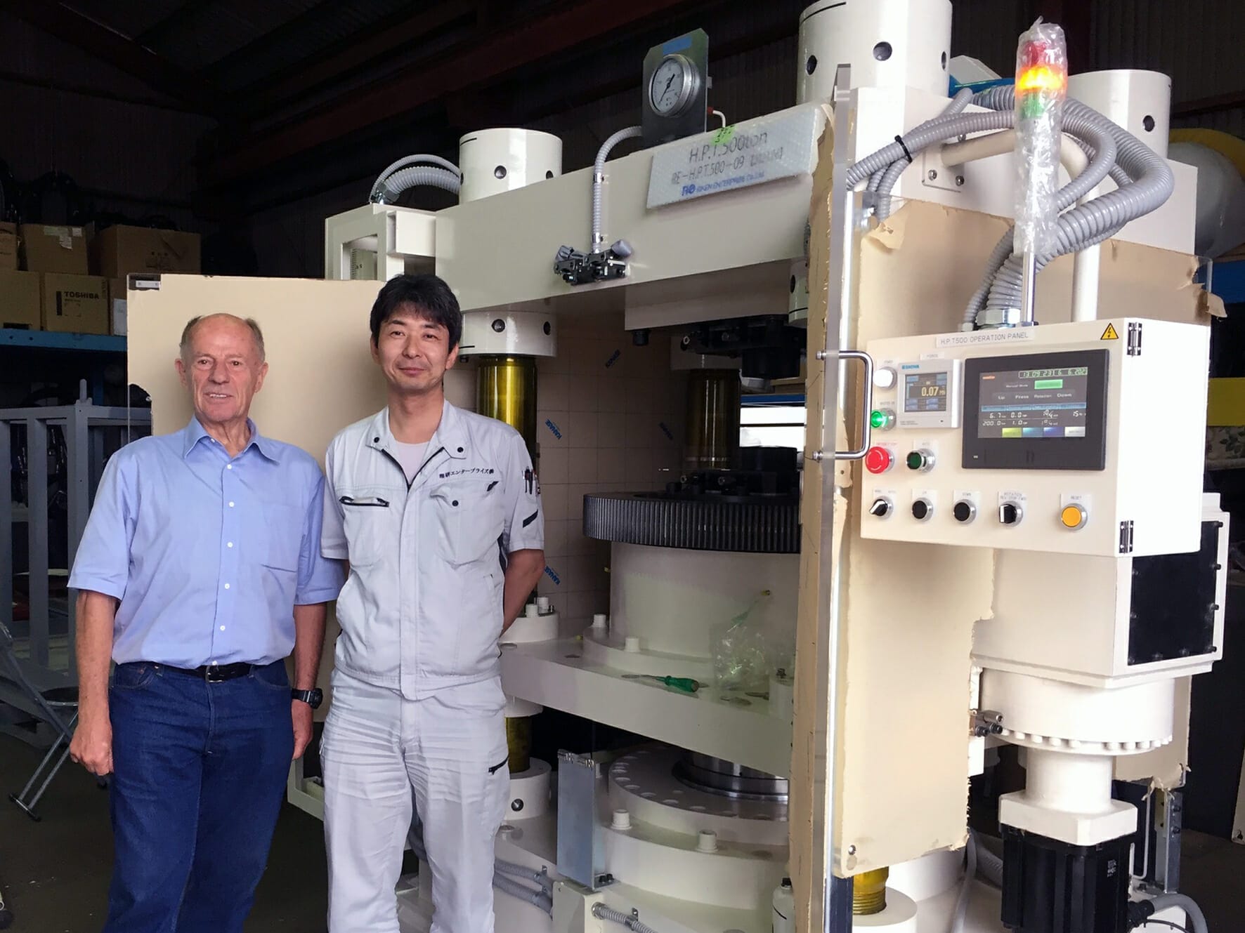 A photograph of 2 men standing in front of a high pressure torsion press